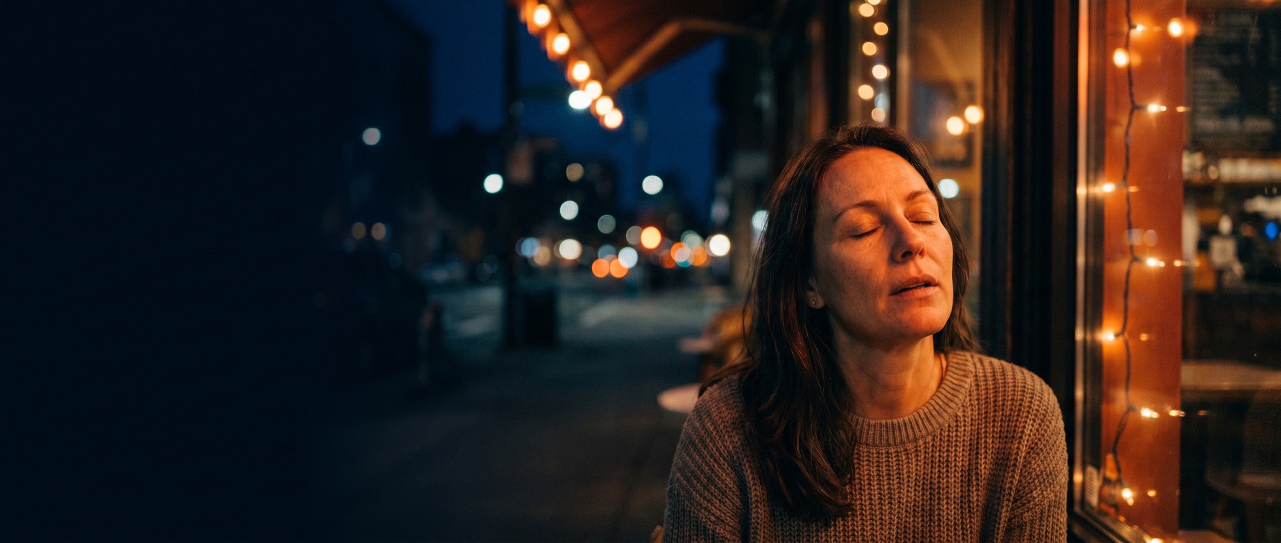 A woman, eyes closed, exhaling in low warm light